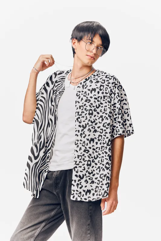 Young man in stylish animal print shirt and glasses posing confidently with modern haircut against a clean white background, showcasing trendy casual fashion.