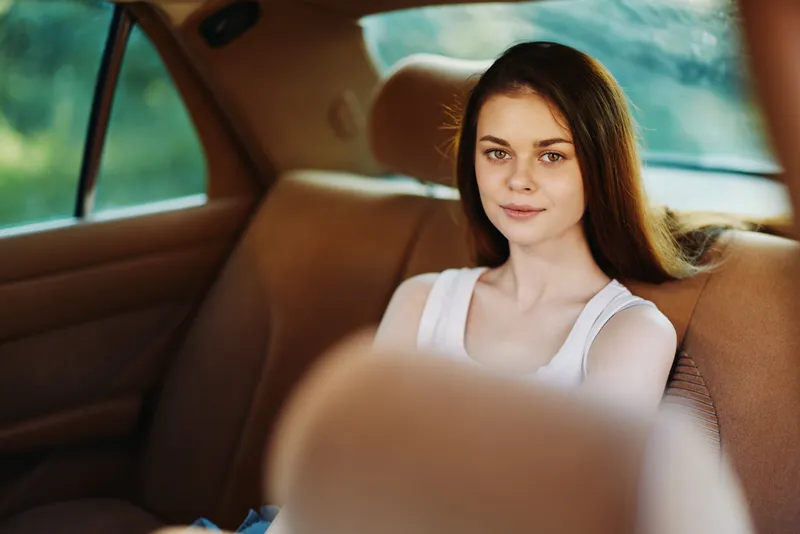 Young woman in casual outfit sitting in the backseat of a car, exuding a calm and thoughtful expression, surrounded by a warm brown interior, suitable for lifestyle themes.
