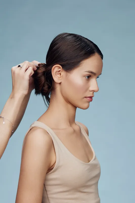 Female model in a beige top with sleek, minimalist hairstyle against a soft blue background, showcasing confidence and elegance for hair styling concepts