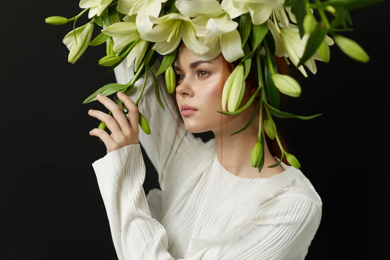 Young woman with vibrant floral headpiece, wearing a cozy white sweater, showcasing serenity with a gentle expression against a dark background