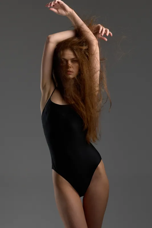 Woman with long hair in black bodysuit posing against gray background, fashion, beauty, style, elegance
