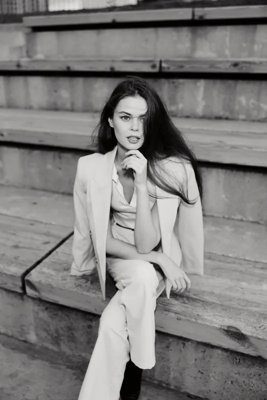 Confident businesswoman in stylish blazer, seated on steps, showcasing modern corporate elegance and sophistication in a monochrome setting.
