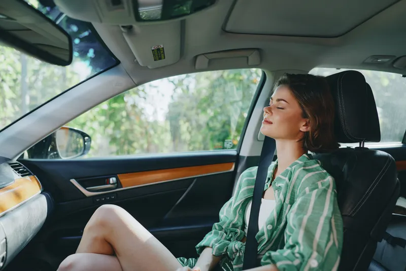 A young woman relaxing in a modern car seat, eyes closed, enjoying a calm moment during a drive.