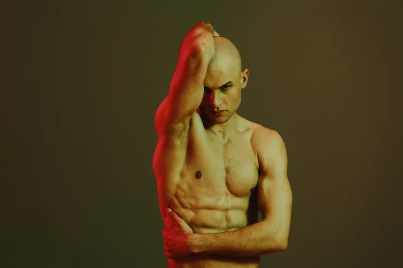 Strong man posing with a confident expression, showcasing toned muscles and an intense vibe. The lighting enhances the dramatic black and white effect.