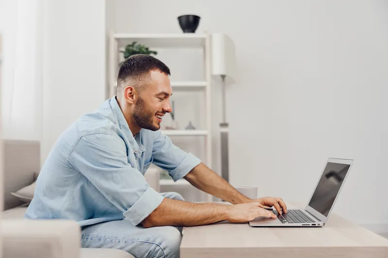 A joyful man working on a laptop at home, embodying a blend of personal and professional life, highlighting the importance of mental health and emotional balance.
