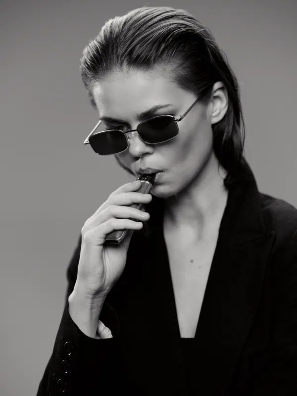 Black and white portrait of a stylish woman wearing sunglasses and a blazer in a contemplative mood.