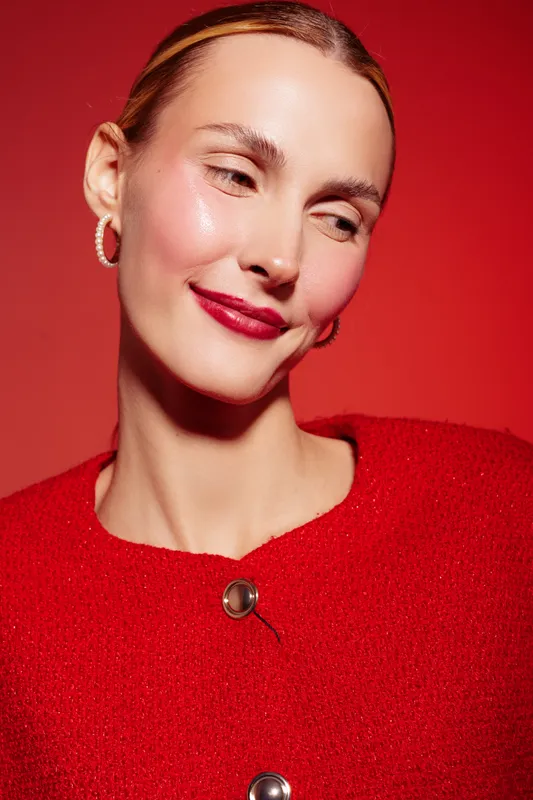 Close-up of a smiling woman with red lipstick and red sweater against red background. Concept of beauty, fashion, makeup, and confident female portrait in studio lighting.