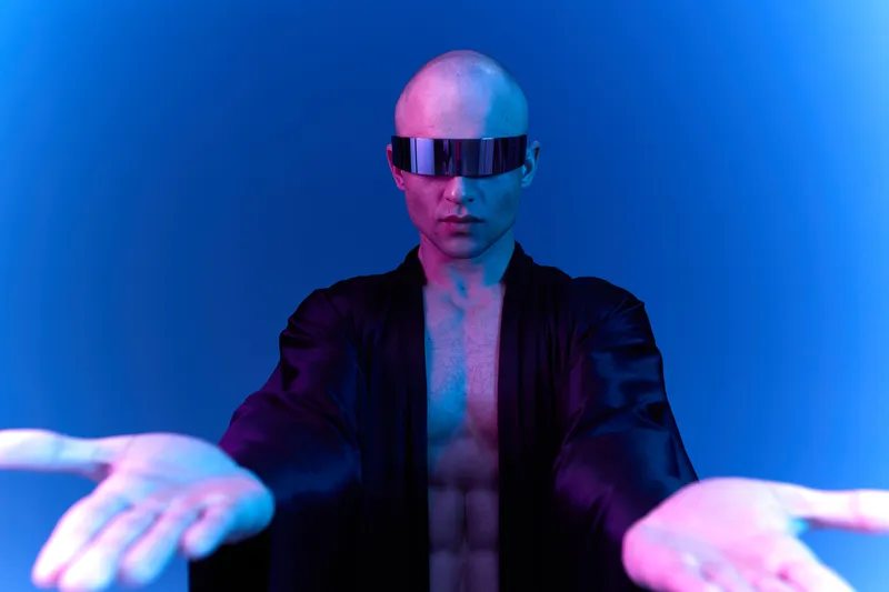 Black and white image of a man with futuristic glasses, extending his arms, showcasing a confident and striking presence in a modern setting.