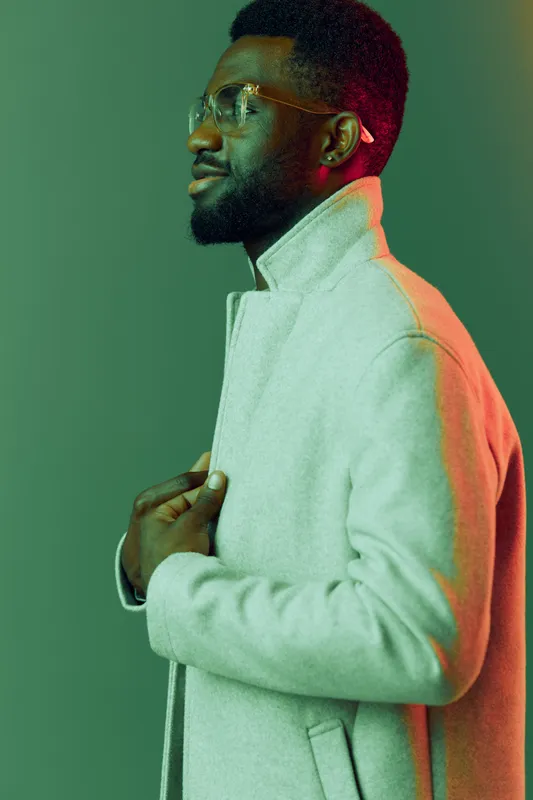 Stylish African man in a trendy gray coat, showcasing confidence and sophistication against a colorful gradient background, perfect for fashion and lifestyle themes