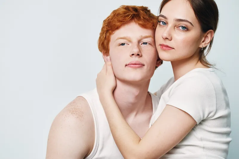 Couple, young man and woman in white tops posing close, intimacy, natural look, relationship, love, studio portrait with plain background and soft lighting.