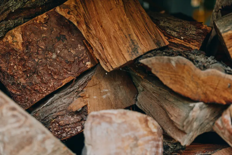 Firewood stacked logs woodpile bark closeup rustic fireplace texture: close-up of chopped hardwood piled for winter, rough bark and grain visible, cozy rural homestead fuel preparation.