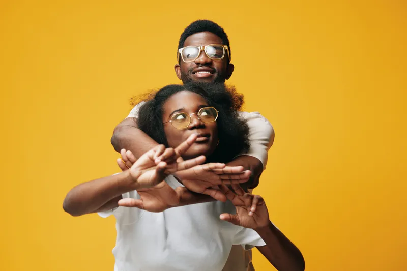 Young African couple embracing on a vibrant yellow background, showcasing joy and connection with stylish eyewear and casual clothing