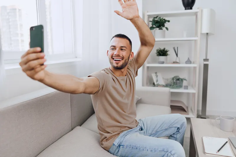 Smiling man taking a selfie in a bright, modern living room, showcasing joy and casual style. Perfect for social media and lifestyle themes.