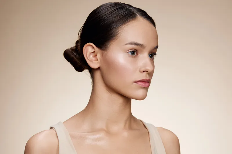 Elegant portrait of a young model with natural makeup, showcasing a serene expression against a soft beige background, emphasizing beauty, confidence, and simplicity