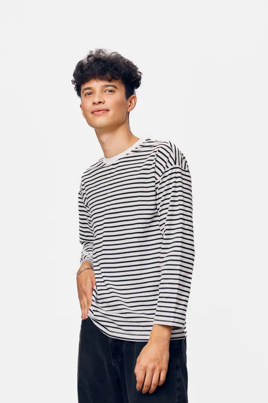 young man wearing striped shirt standing casually with hand in pocket, looking confident against white background in modern casual style