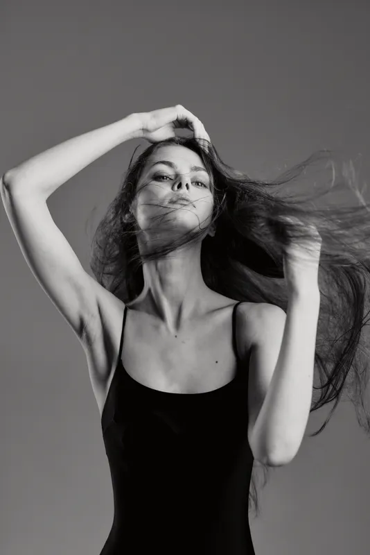 Black and white portrait of a young woman in a black dress with flowing hair, expressing elegance and motion.