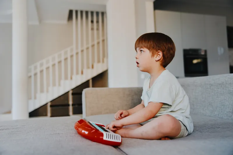 Curious boy playing with a toy keyboard, focused expression and casual attire, indoor setting with soft lighting, creating a warm atmosphere.
