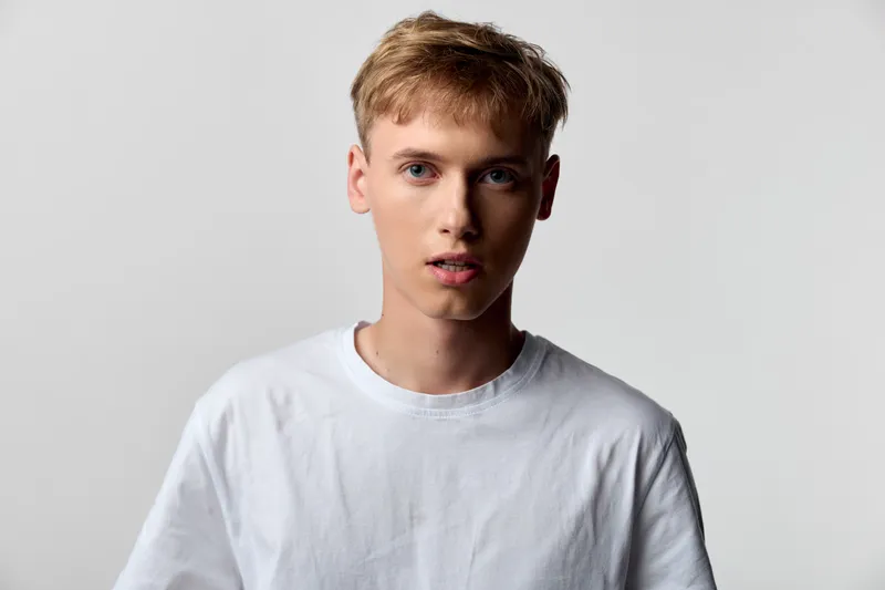 Young man, male model in a white tee stands in a studio with a neutral background, offering a clean minimal look suitable for fashion, lifestyle, and advertising uses