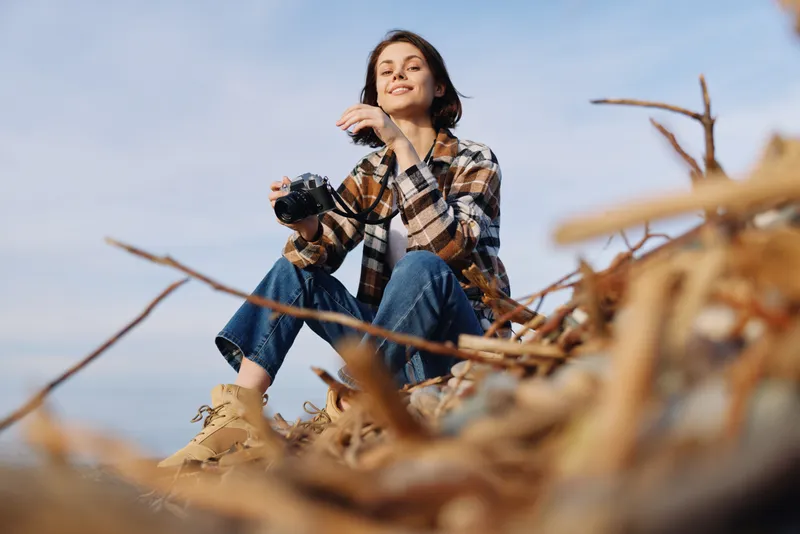 Photography of a photographer resting among beach reeds with a camera, enjoying outdoor leisure and candid moments. A calm portrait moment against scenic coast, sunlight and wind creating a relaxed,