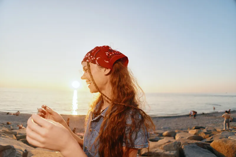 lifestyle woman in modern boho-western denim street style enjoying sunset by the beach with film color warm tones and casual relaxed mood