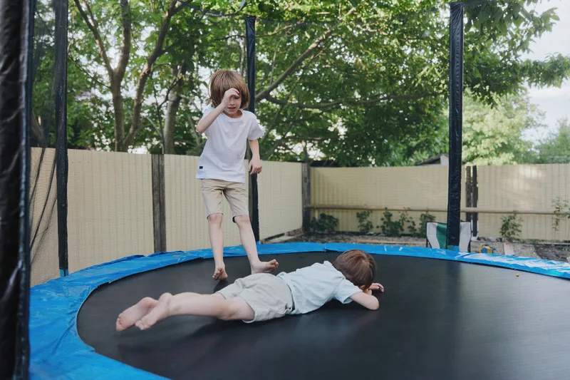 Active boys playing on a trampoline, enjoying the sunny day outdoors with laughter and excitement, perfect for capturing childhood joy and energy. ###