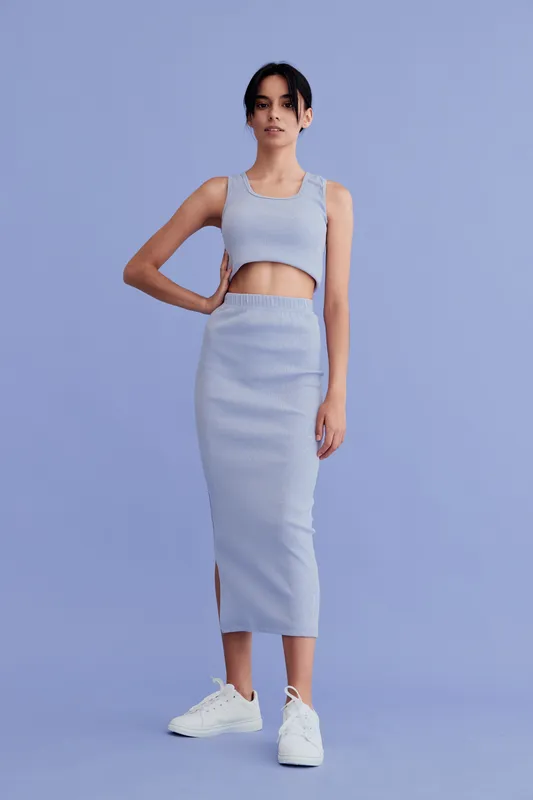 Young woman in stylish light blue two-piece outfit and white sneakers poses confidently against a soft blue background, showcasing modern casual fashion and minimalistic style.