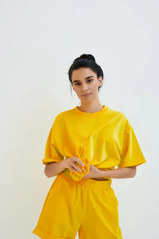young woman in bright yellow casual outfit posing indoors, minimalistic white background, relaxed expression, sporty style, comfortable clothing