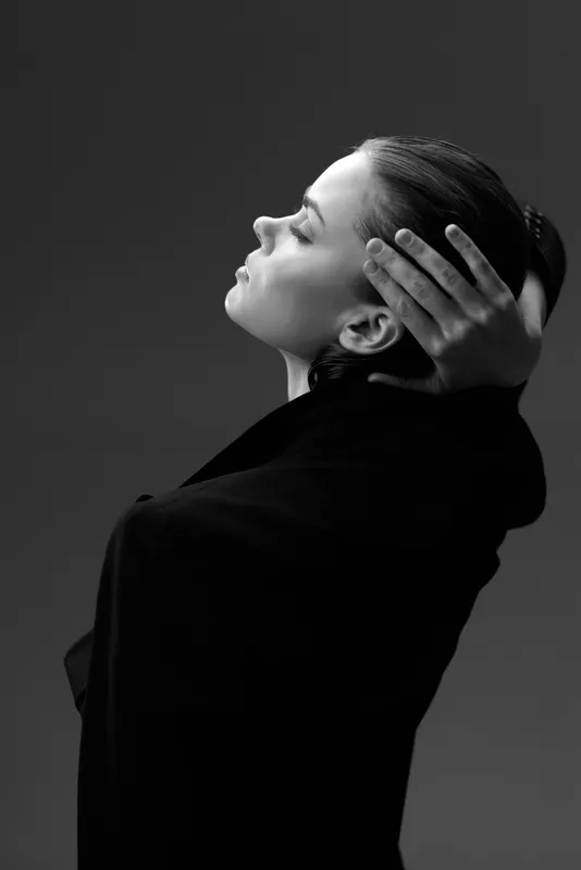 Black and white portrait of a woman with closed eyes, serene expression, and hands near face in studio lighting.