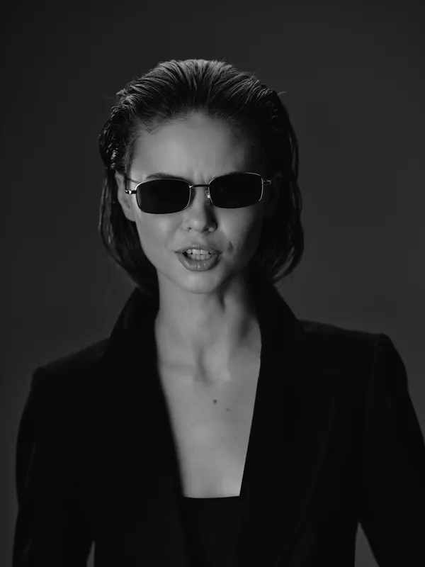 Confident woman wearing sunglasses and black blazer in black and white portrait with moody atmosphere