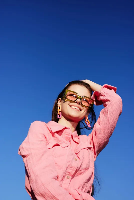 Young woman smiling in vibrant pink outfit against clear blue sky, expressing joy and confidence perfect for lifestyle and fashion related concepts