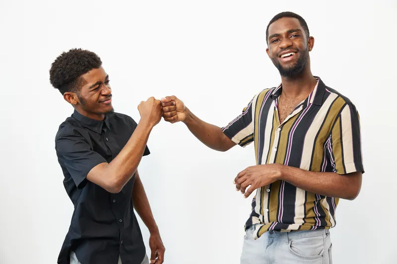 Two smiling African American men sharing a joyful fist bump, showcasing friendship and positivity in a bright, casual setting.