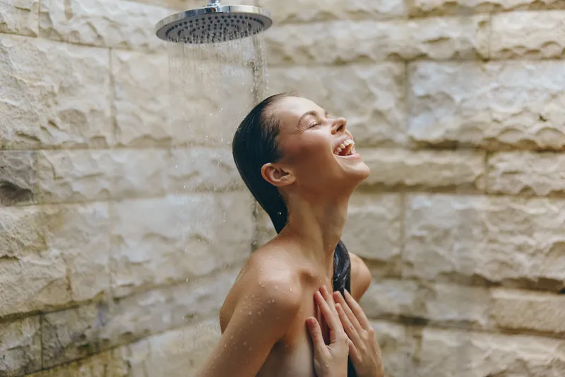 happy woman enjoying outdoor shower with wet hair, natural stone wall background, bright and refreshing moment, summer joy and relaxation