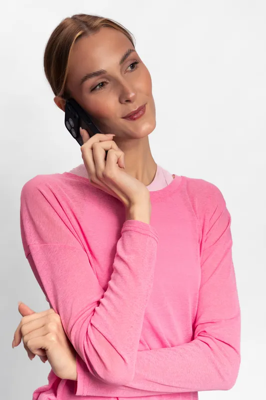 Young woman in pink sweater talking on phone with thoughtful expression against white background. Concept for communication, lifestyle, casual and modern technology usage.