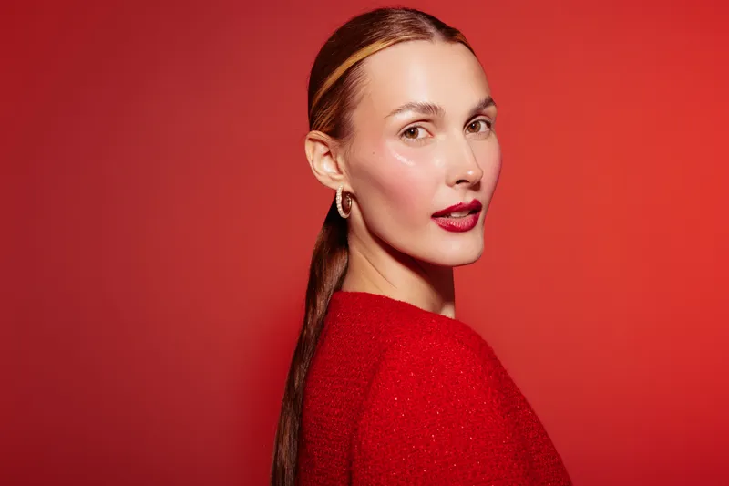 Portrait of a confident woman with red lipstick and sleek hair wearing a red sweater against a red background. Concept of beauty, fashion, and elegance in studio lighting.