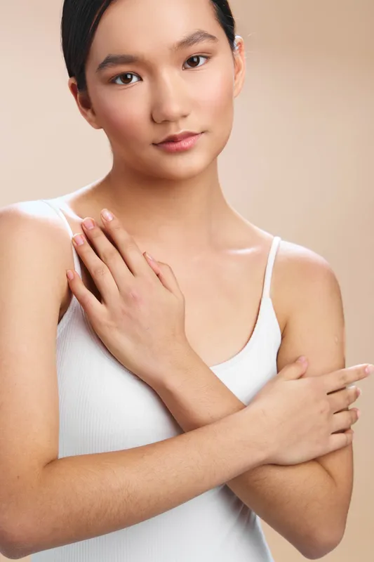 asian woman in a minimalist studio poses with arms crossed, presenting a calm, confident expression and warm presence against a neutral backdrop, ideal for professional lifestyle imagery.
