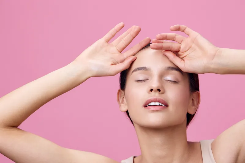 Young woman with closed eyes expressing tranquility against a pink background, showcasing healthy skin and a serene mood in a minimalistic style