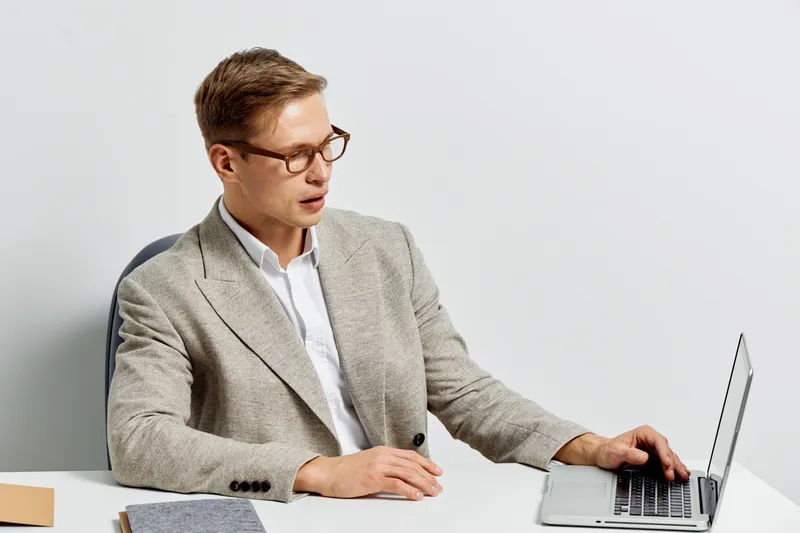 focused caucasian man working laptop business casual wear eyeglasses sit at table plain background digital nomad concept