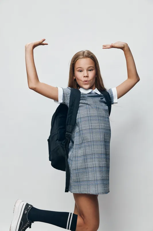Girl, school, backpack, arms, standing and posing in studio. Student in dress with black backpack showing height with hands on white background.