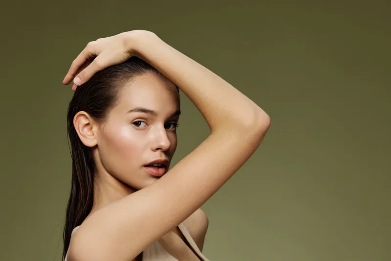 Portrait of a young woman with long hair, showcasing a serene expression against a soft green background, embodying natural beauty and simplicity