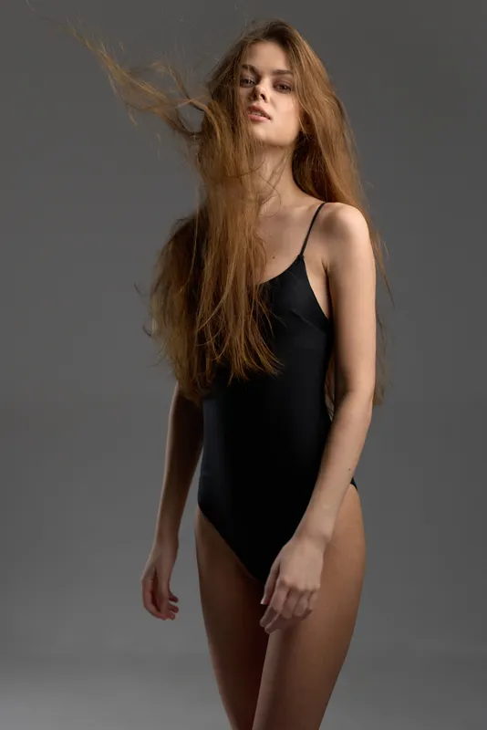 young woman in black bodysuit with flowing hair standing on gray background, fashion, elegance, confidence