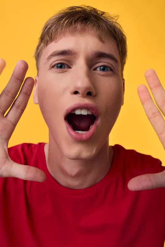 Surprised man with hands up in a bold studio shot, bright yellow background and red shirt conveying excitement, energy, and playful mood for dynamic marketing or creative campaigns