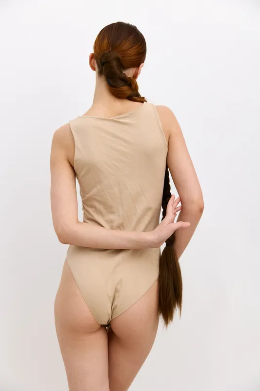 woman with long braided hair wearing beige bodysuit standing against white background, back view, minimalistic style, natural lighting, simple composition