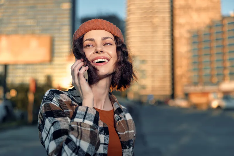 Woman on phone with smile in urban street at golden hour sunlight, candid lifestyle portrait conveying authenticity, mindful living and emotional storytelling with warm glow.