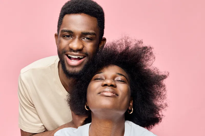 Happy young African American couple smiling against a pink background, showcasing love and joy in a vibrant, fun, and colorful atmosphere, perfect for celebrating relationships