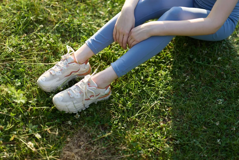 Young woman in activewear sitting on grass, wearing stylish sneakers, expressing relaxation, embodying a healthy lifestyle, vibrant spring colors