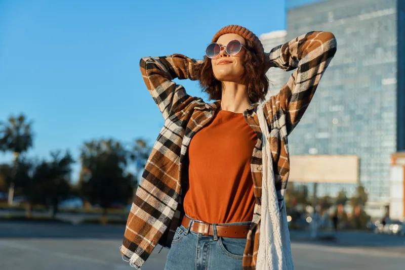 woman sunglasses beanie plaid sunlight city candid lifestyle portrait in golden hour glow, authenticity and mindful living reflected in relaxed pose and emotional storytelling mood