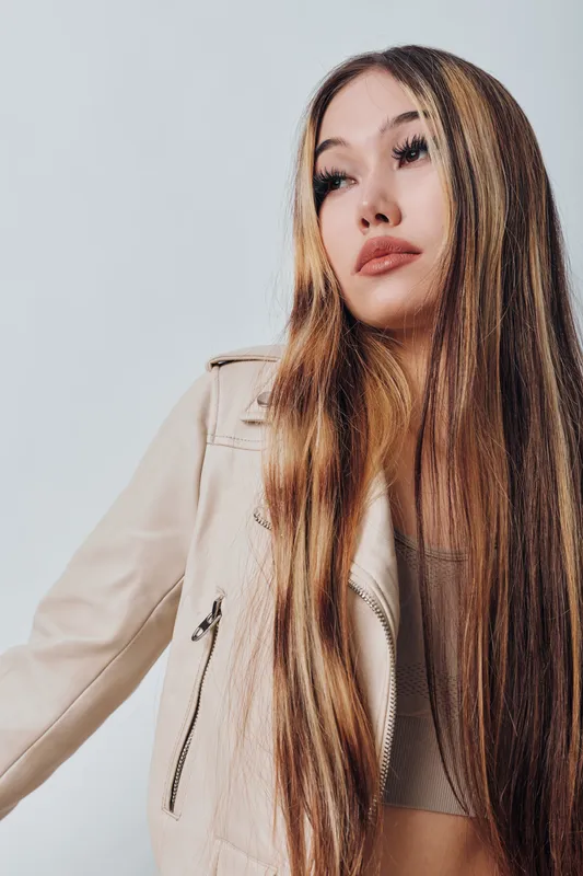 Young woman with long hair wearing beige jacket and white top posing against light background. Stylish casual outfit and natural makeup with serious expression closeup portrait.