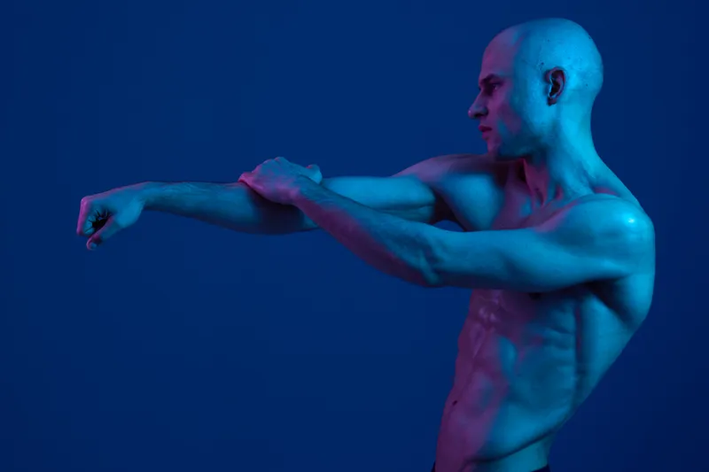 Athletic man stretching in a cool blue light, showcasing his toned physique. This black and white image emphasizes strength and determination in motion.
