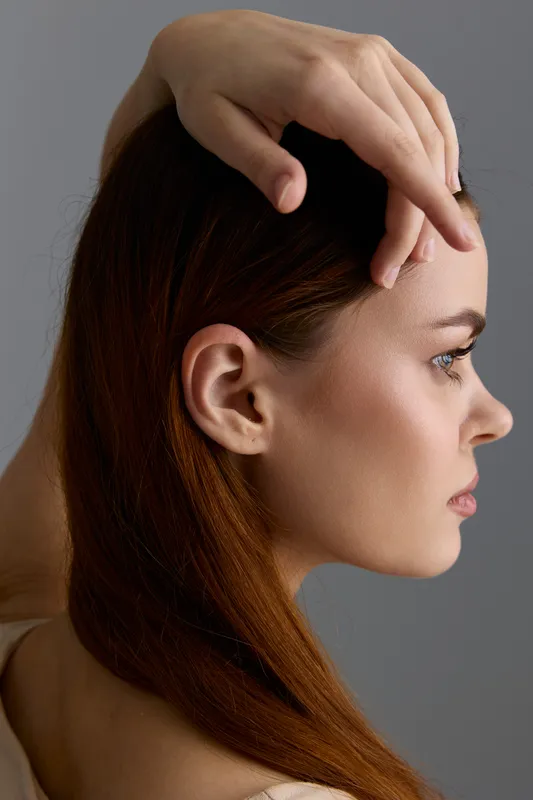 Beauty woman with red hair in profile pose showcasing smooth skin and natural makeup against a neutral gray background, embodying elegance and modern fashion style.