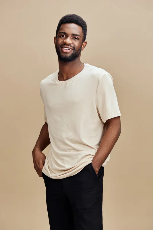 Smiling African American man in a casual beige t shirt poses against a warm brown background, showcasing a relaxed and confident style perfect for lifestyle representation